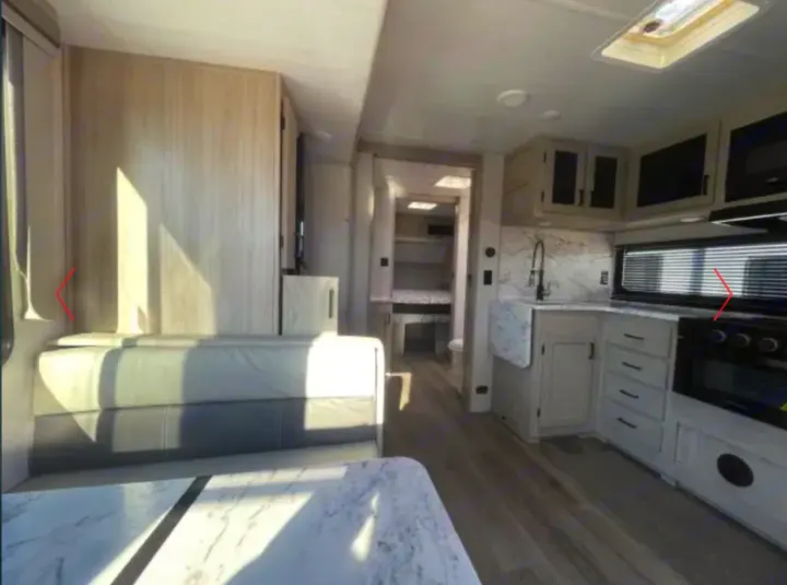 Inside a bright RV rental: modern kitchen, dinette seating, and hallway leading to a sleeping area.. Alto East West 2024