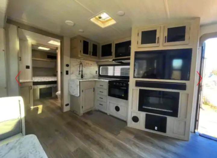 Modern RV rental interior: kitchen, living area with TV/fireplace, and partial bedroom view through an open doorway.. Alto East West 2024