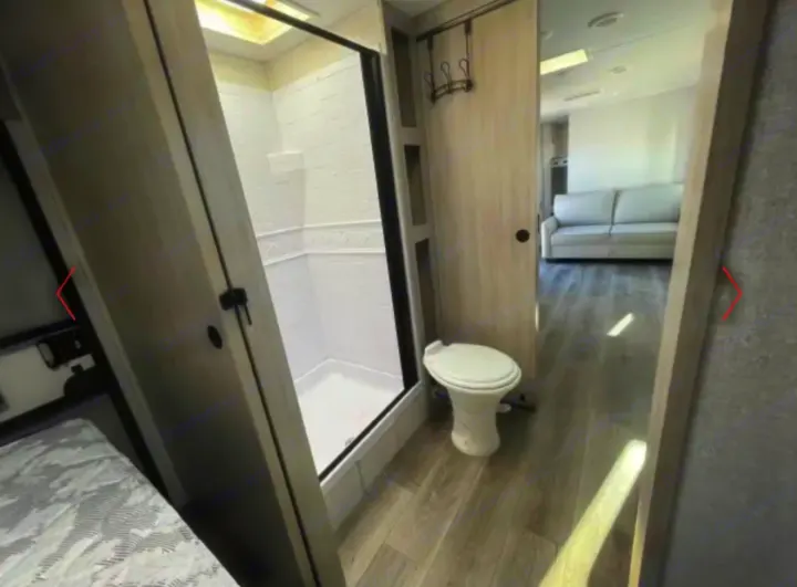 RV rental interior featuring a compact bathroom with a shower and toilet, plus a visible living area with a couch.. Alto East West 2024