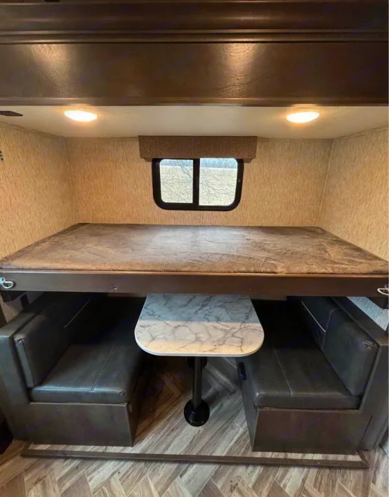 This RV rental interior shows a bunk bed over a dinette with a marble table and dark upholstered seating.. Astoria Astoria Trailer 2022