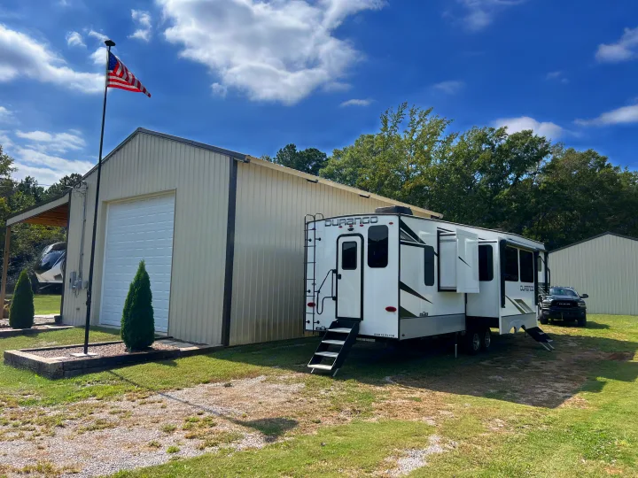 Spacious Durango fifth-wheel rv rental, parked by a metal building with an American flag. A truck is visible behind.. Durango Durango Fifth Wheel 2023