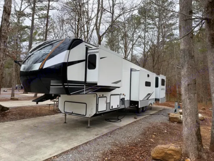 Spacious fifth-wheel RV rental parked at a serene campsite with trees, its slide-outs extended for extra room.. Durango Durango Fifth Wheel 2023