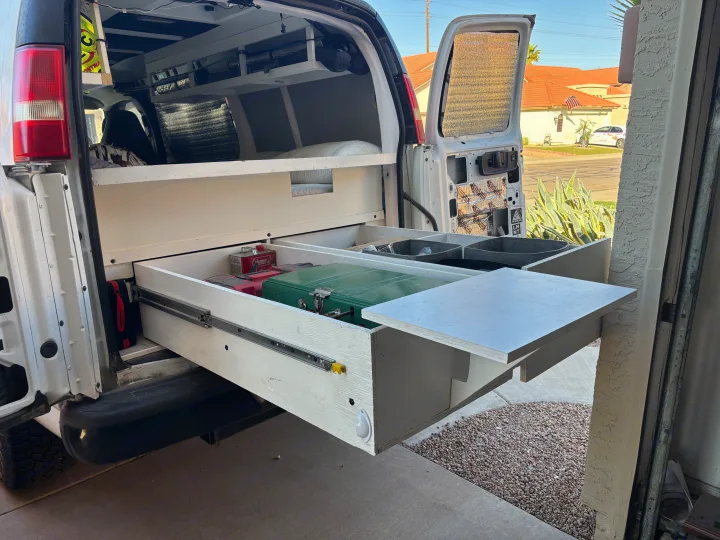 Customized RV rental camper van interior featuring a pull-out kitchen drawer, stove, and organized storage.. Chevrolet Express 1500 AWD 2007