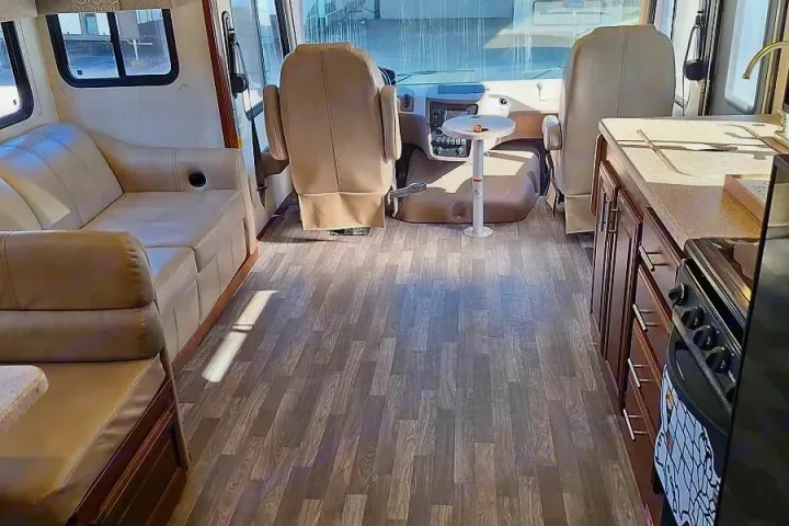 Bright, clean RV rental interior with wood-look flooring, ample seating, and a functional kitchen. Driver's cockpit visible.. FR3 FR3 Motorhome 2018
