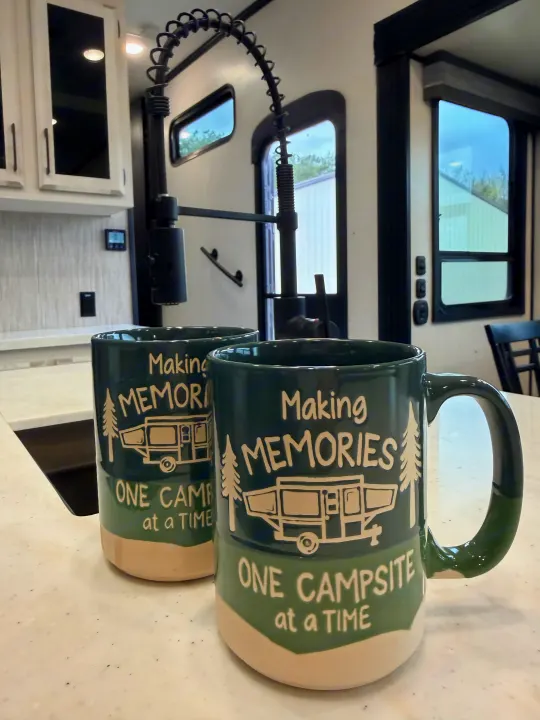 Two "Making Memories" mugs featuring a camper and trees sit on a counter in a modern RV rental kitchen.. Durango Durango Fifth Wheel 2023