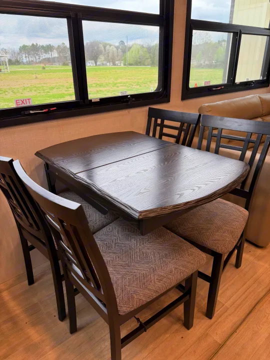 RV rental dining space with a dark wood table, four patterned chairs, and large windows revealing a green outdoor view.. Durango Durango Fifth Wheel 2023