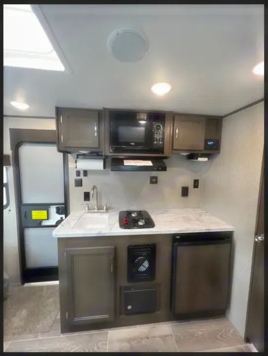 RV rental kitchen view: compact space with sink, two-burner stove, microwave, fridge, and overhead cabinets.. Jayco Jay Flight SLX Baja Edition 2021