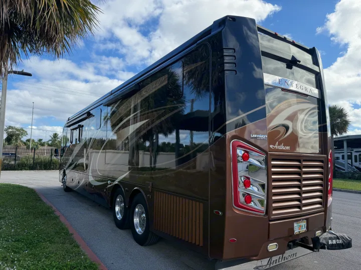 This large, brown Entegra Anthem luxury rv rental is parked outside. Palm trees reflect on its glossy side under a blue sky.. Entegra Coach Anthem 2019