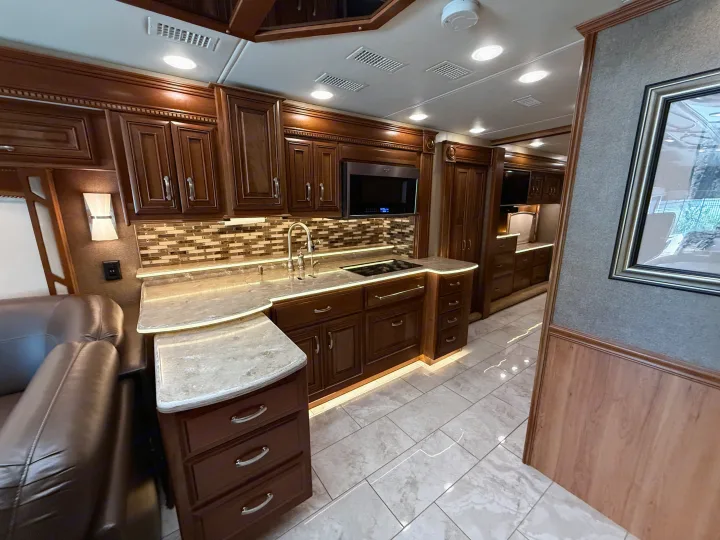 Luxurious RV rental kitchen with dark wood cabinetry, light countertops, modern appliances, and ambient LED lighting.. Entegra Coach Anthem 2019