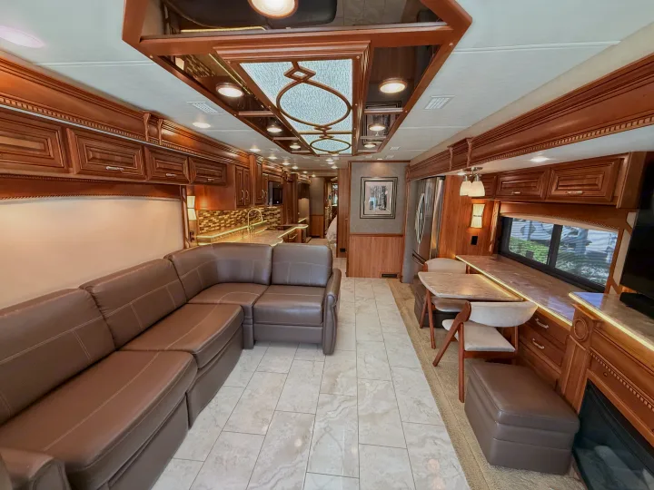 Spacious, luxurious rv rental interior with a comfy brown sectional sofa, modern kitchen, dining area, and fireplace feature.. Entegra Coach Anthem 2019