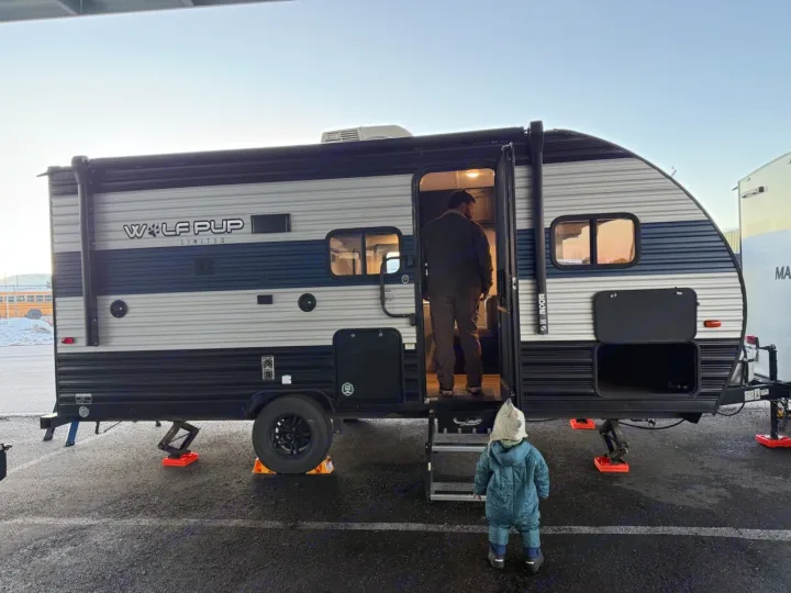 A man stands inside a Wolf Pup rv rental, seen from behind, as a small child looks up from outside. Ready for camping adventure.. Forest River Cherokee Wolf Pup 2021