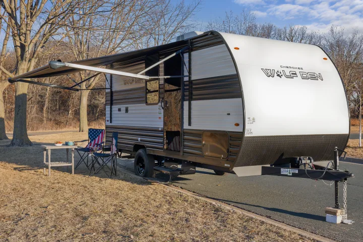 This RV rental, a Cherokee Wolf Den travel trailer, features a cozy outdoor setup with chairs and a table under its awning.. Forest River Wolf Den 16EV 2025