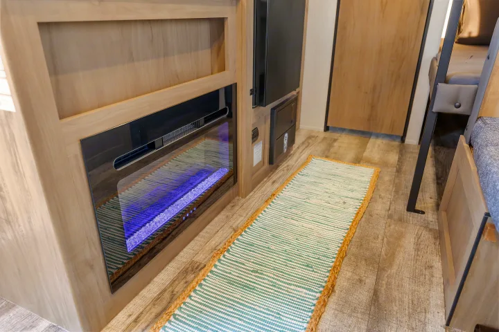 RV rental living space featuring a glowing electric fireplace, light wood cabinetry, a colorful floor runner, and practical flooring.. Forest River Wolf Den 16EV 2025