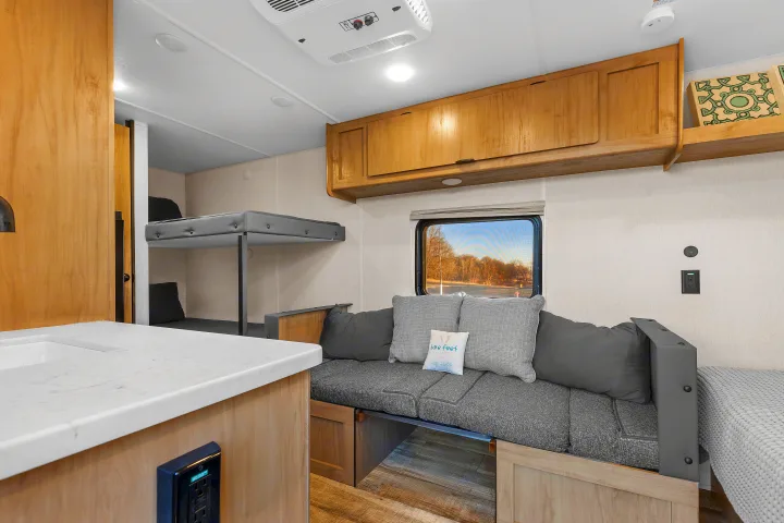 Spacious RV rental interior with light wood cabinetry, bunk beds, and a comfy dinette with cushions. Sink and window also visible.. Forest River Wolf Den 16EV 2025