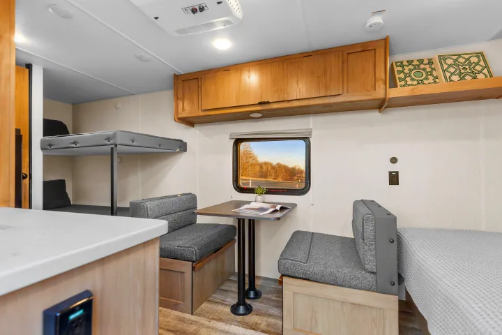 Cozy RV rental interior: dining area with window, bunks, and kitchen counter visible. Functional space for travelers.. Forest River Wolf Den 16EV 2025