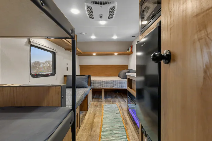 View inside an RV rental, showcasing compact bunk beds, a main bed, and a refrigerator. Well-designed, functional interior.. Forest River Wolf Den 16EV 2025