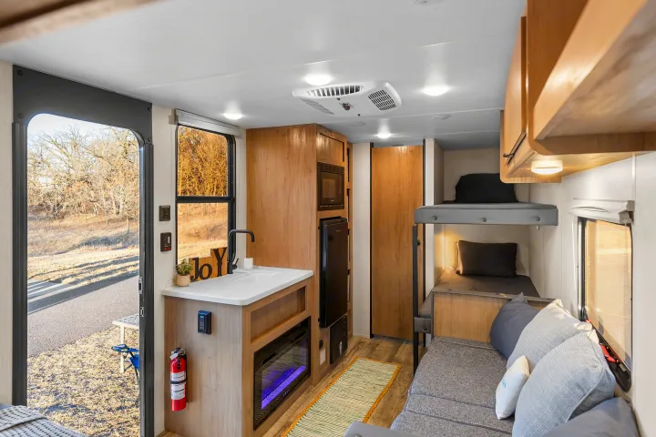 Step inside this RV rental, showcasing a functional kitchen, comfy bunk beds, and a sofa by an open door to nature.. Forest River Wolf Den 16EV 2025
