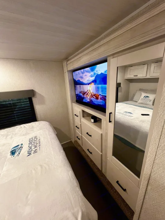 Cozy RV rental bedroom with TV, storage, and a comfy bed with "Memories in Motion" branding, reflecting in the mirrored closet.. 1FDXE4FN9RDD14726 3100FB 2023