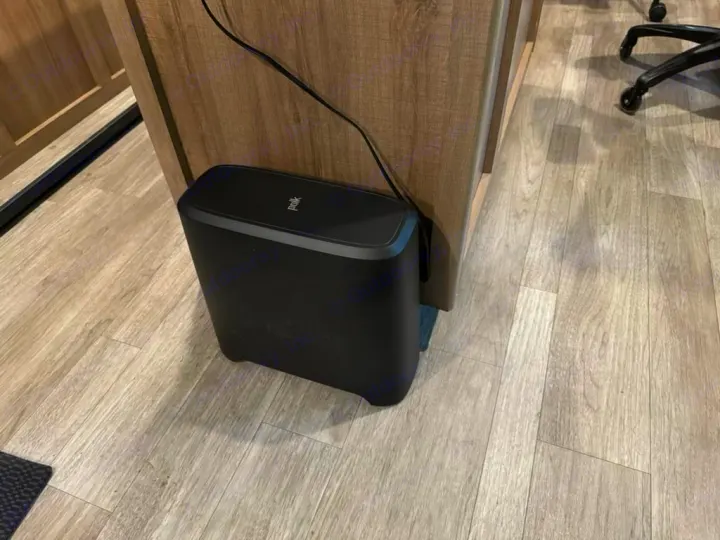A sleek black Polk subwoofer on light wood flooring, nestled against a cabinet, enhancing audio in an RV rental.. Grand Design Imagine 2023