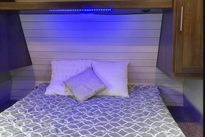 Cozy RV rental bedroom with blue LED lighting, white/grey bedding, light paneled headboard, and wood accents.. Crossroads RV zinger 2019