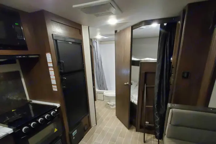 RV rental interior featuring a kitchen with fridge, bathroom with shower, and bunk beds. Compact travel trailer design.. Forest River Cherokee Grey Wolf 2020