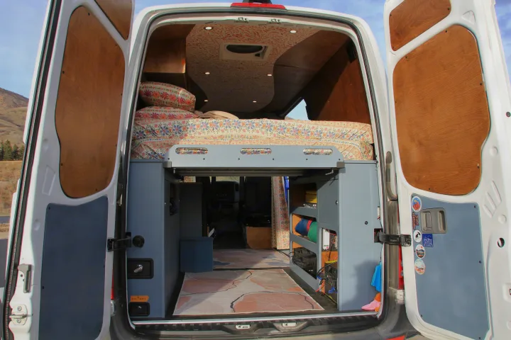 Customized RV rental interior viewed from the rear doors, showing a floral bed, patterned ceiling, and storage.. Mercedes-Benz Sprinter 2018