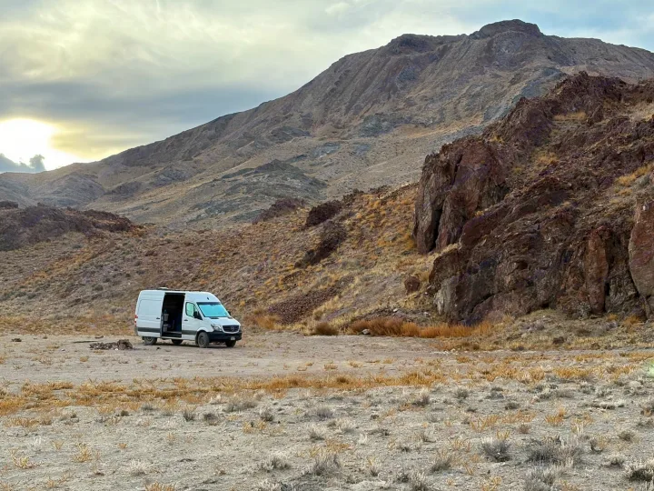 Adventure-ready rv rental: A white camper van parked in a rugged desert mountain landscape under a bright, cloudy sky.. Mercedes-Benz Sprinter 2018