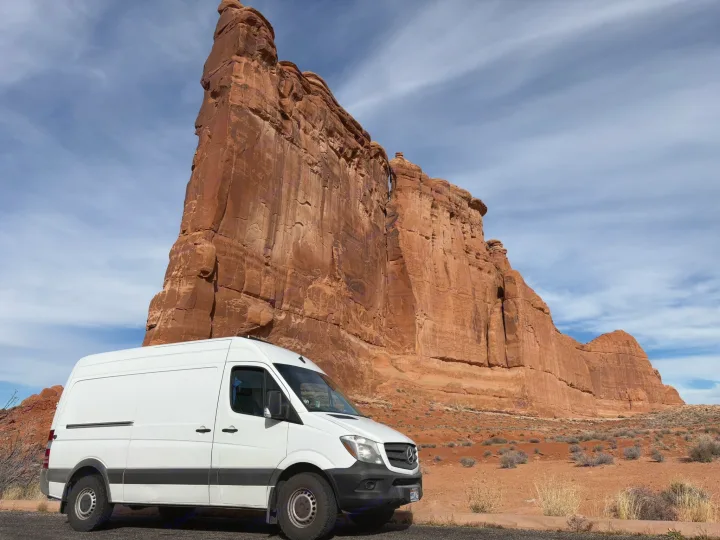 White Sprinter rv rental parked by a colossal red rock formation in a national park. Ideal for desert road trips.. Mercedes-Benz Sprinter 2018