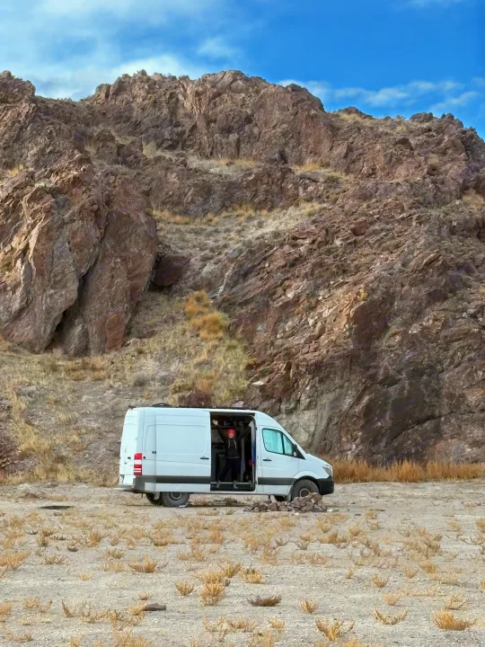 Adventure awaits! White camper van parked against rocky mountains, a person cheering from inside. Ideal rv rental for exploring nature.. Mercedes-Benz Sprinter 2018