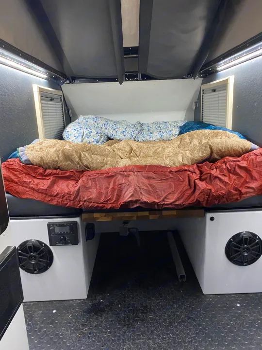 Cozy rv rental sleeping area features a bed with layered bedding, integrated lighting, side vents, and a compact audio system.. Mission Overland Mission Overland Trailer 2023