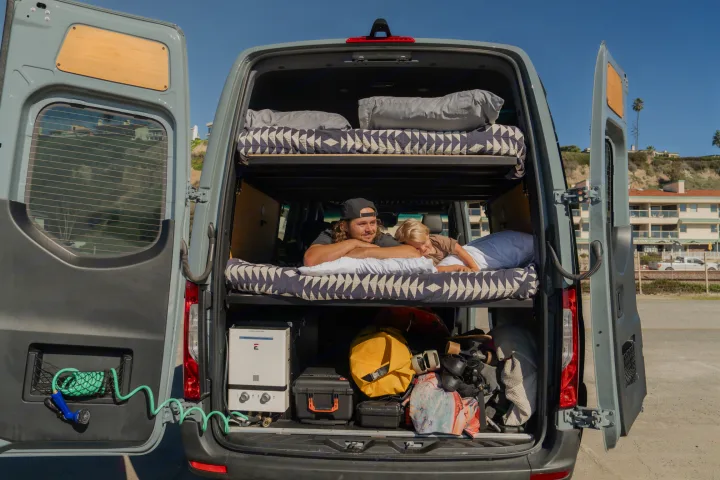 RV rental's open back reveals bunk beds with a man & child, gear storage, and a coiled hose for adventure.. Mercedes sprinter 2025
