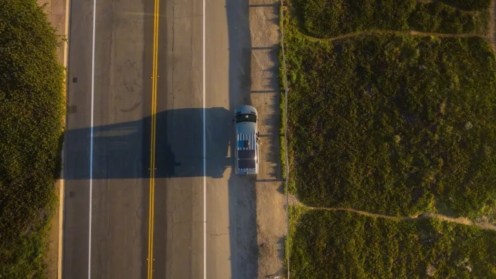 Aerial view of an RV rental parked roadside during golden hour. Lush greenery borders the road, with shadows stretching across the pavement.. Mercedes sprinter 2025