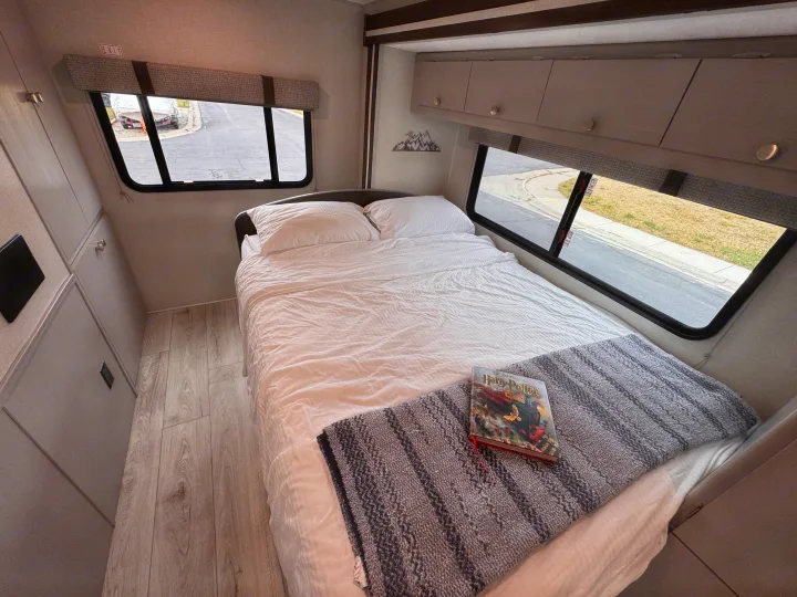 Cozy RV rental bedroom with a comfortable bed, overhead storage, and a Harry Potter book for relaxing on your travels.. Forest River Coachmen Freelander 2026