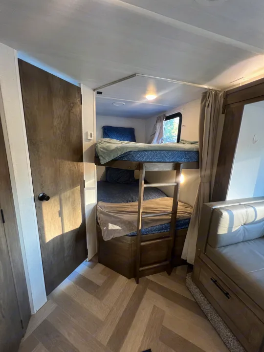 RV rental interior featuring cozy bunk beds with a ladder, window, and adjacent seating area.. Forest River Wildwood X-Lite 2020