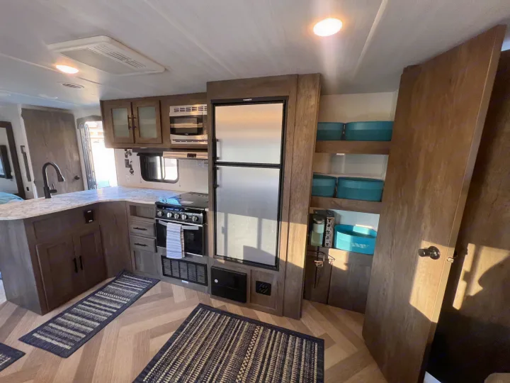 Modern RV rental kitchen: dark cabinets, full appliances including fridge, stove, microwave, and shelving with storage bins.. Forest River Wildwood X-Lite 2020