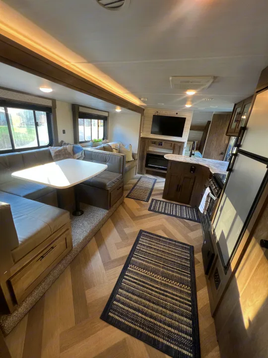 Bright RV rental interior: dinette, kitchen with stove/fridge, living area with TV & fireplace, herringbone floors.. Forest River Wildwood X-Lite 2020