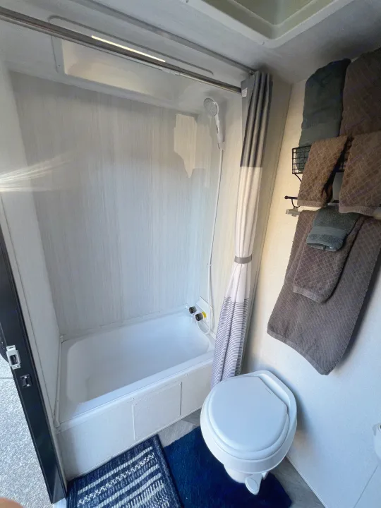 Inside this RV rental, find a compact bathroom with a white tub, shower, toilet, and convenient towel rack.. Forest River Wildwood X-Lite 2020