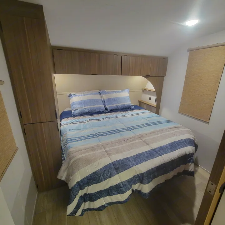 RV rental bedroom featuring a comfy bed with striped blue and beige bedding, built-in wooden cabinets, and a ceiling light.. Forest River Salem Cruise-Lite 2026