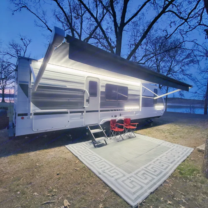Lit rv rental parked at a serene lakeside campsite at dusk, with an extended awning, chairs, and outdoor mat.. Forest River Salem Cruise-Lite 2026