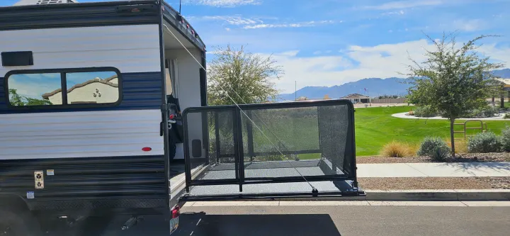 RV rental toy hauler with patio deck deployed, revealing an ATV inside. Scenic park and mountain backdrop.. Forest River Cherokee Grey Wolf 2023