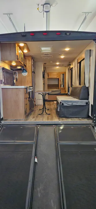 RV rental: Inside a toy hauler, showing its kitchen, living area with sofa, and sleeping quarters, viewed from the open rear ramp.. Forest River Cherokee Grey Wolf 2023