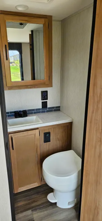 This RV rental bathroom features a sink, mirror, toilet, and wooden vanity, offering essential amenities in a compact space.. Forest River Cherokee Grey Wolf 2023