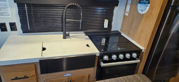 Compact RV rental kitchen setup: sleek black sink, spring faucet, and a black Girard gas range/oven unit with a cover.. Forest River Cherokee Grey Wolf 2023