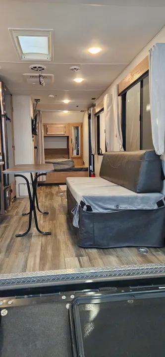 Inside a well-equipped rv rental: dining table, upholstered sofa, bunk beds, and kitchen amenities in a bright, wood-floored space.. Forest River Cherokee Grey Wolf 2023