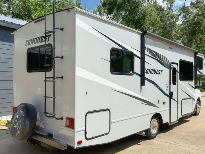 White Conquest Class C RV, ideal for rv rental. Features ladder, awning, and "Life is better at the campsite" spare tire cover.. Conquest 6280 2024