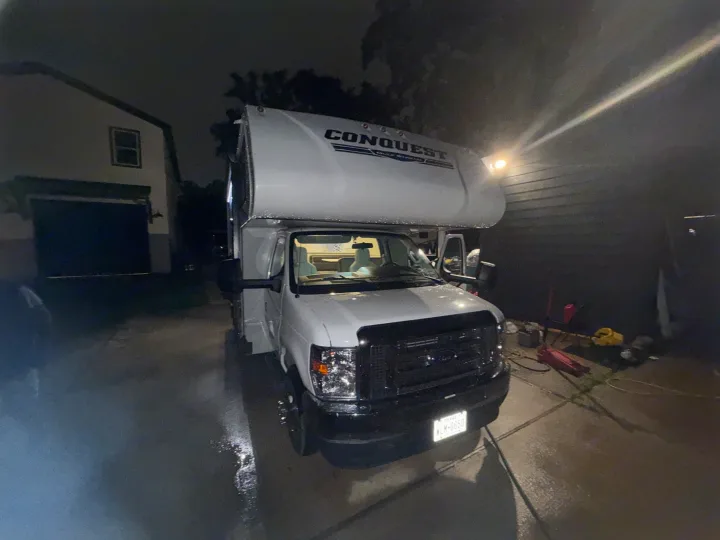 This white Gulf Stream Conquest RV rental, a Class C motorhome, is parked on a wet driveway at night, near a house.. Conquest 6280 2024