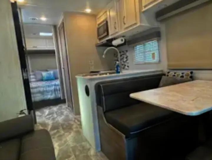 RV rental interior: modern kitchen area with sink, dining booth, and bedroom in the background.. Conquest 6280 2024