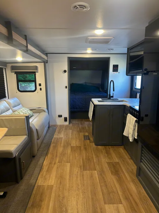 Inside a modern rv rental: kitchen, living room with sofa, and bedroom access. Cozy interior for your adventures.. Keystone RV Bullet Crossfire 2024