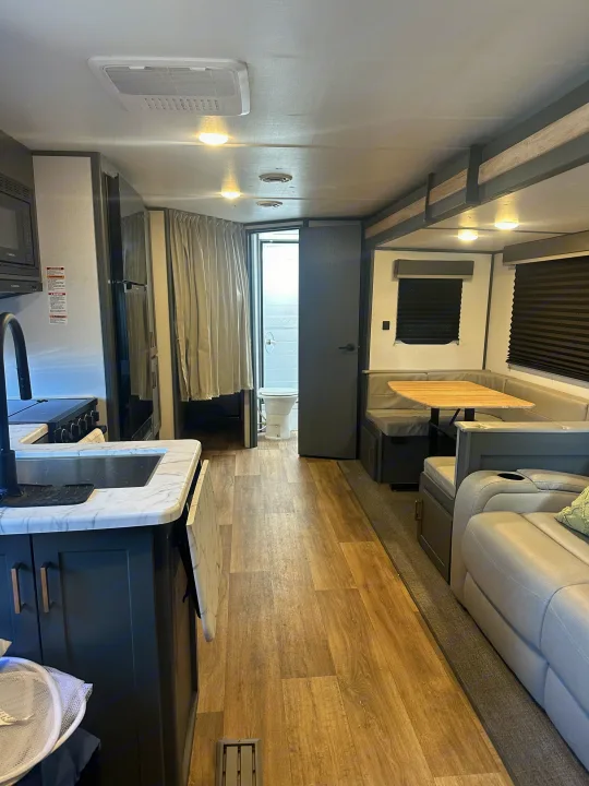 This modern rv rental interior features a full kitchen with dark cabinets, a cozy dinette, and an open bathroom.. Keystone RV Bullet Crossfire 2024