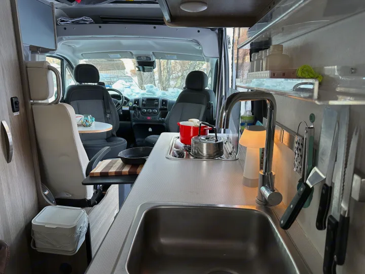 Cozy rv rental kitchen with sink, stove, and cooking tools. View of snowy landscape from driver's area, perfect for winter travel.. Winnebago Solis 2022